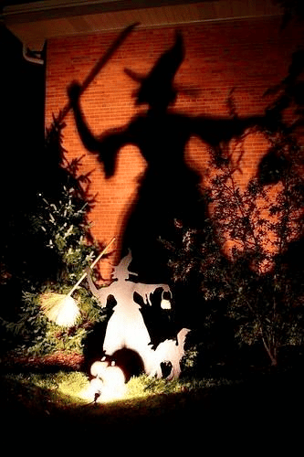 Witch statue illuminated to cast a large shadow